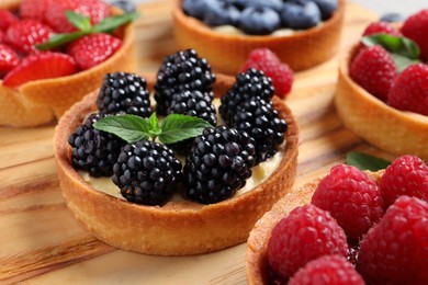 Photo of Tartlets with different fresh berries on wooden board, closeup. Delicious dessert