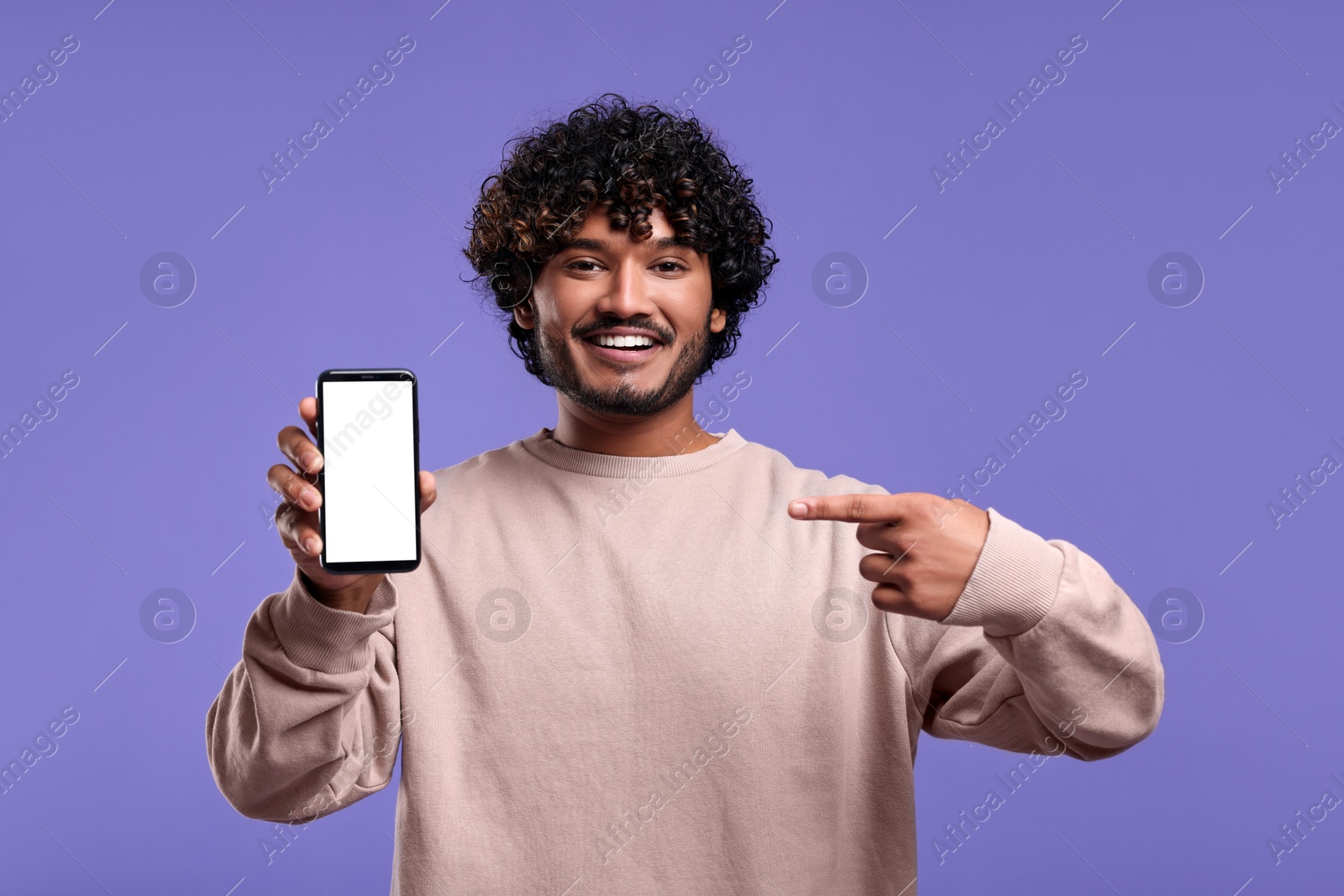 Photo of Handsome smiling man showing smartphone on violet background