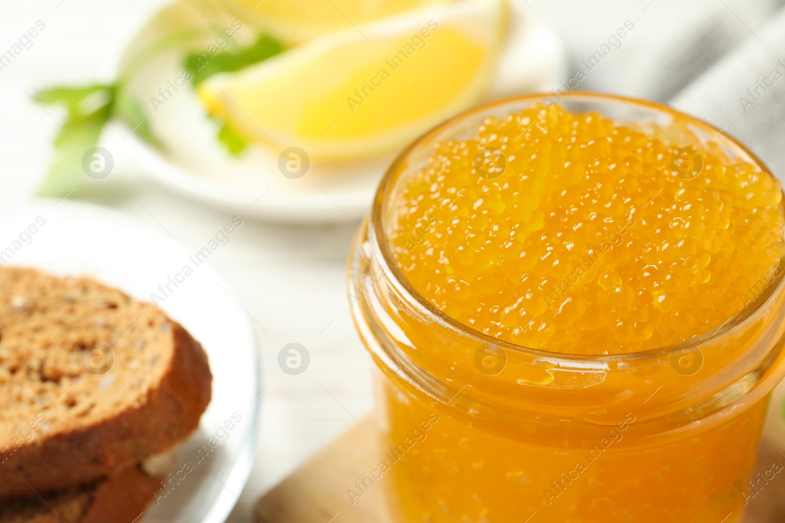 Photo of Fresh pike caviar in glass jar and bread on white wooden table, closeup