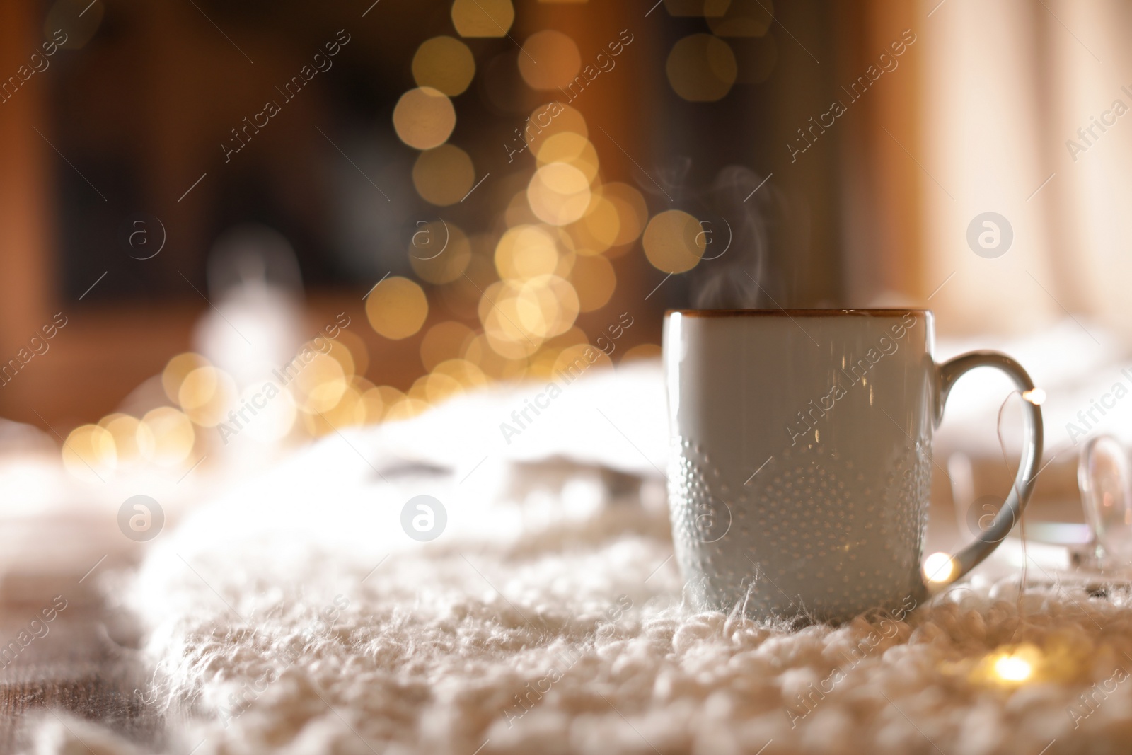 Photo of Cup of hot beverage on fuzzy rug against blurred background, space for text. Winter evening