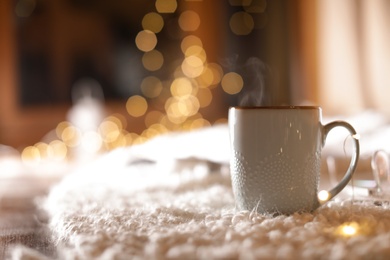 Photo of Cup of hot beverage on fuzzy rug against blurred background, space for text. Winter evening