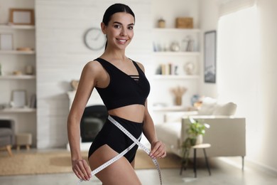 Young woman measuring waist with tape at home. Space for text