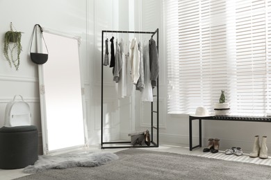 Rack with stylish women's clothes and large mirror in dressing room. Interior design