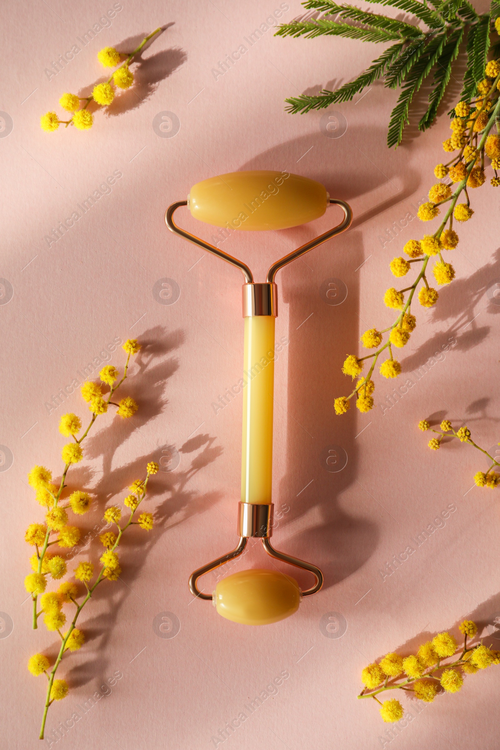 Photo of Natural face roller and flowers on pink background, flat lay