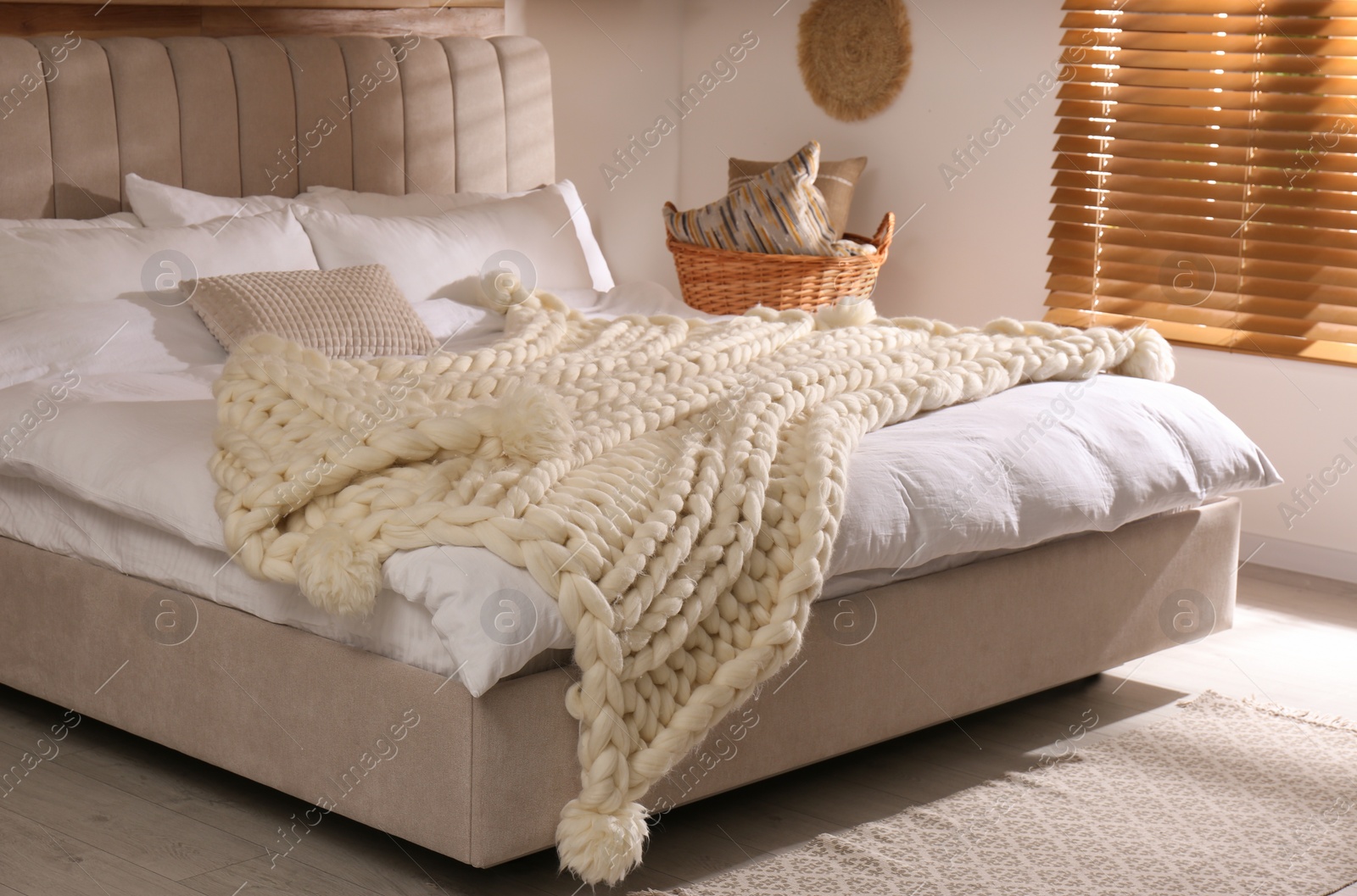 Photo of Bed with white knitted plaid indoors. Interior design