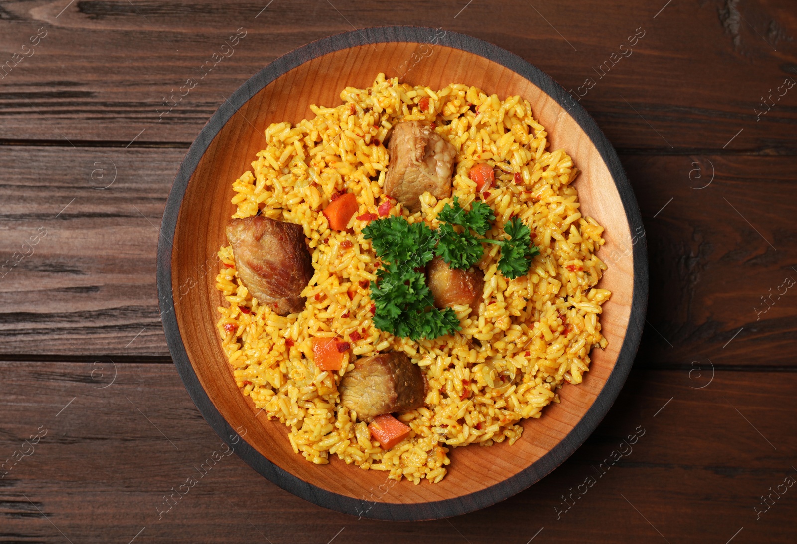 Photo of Plate with rice pilaf and meat on wooden background, top view