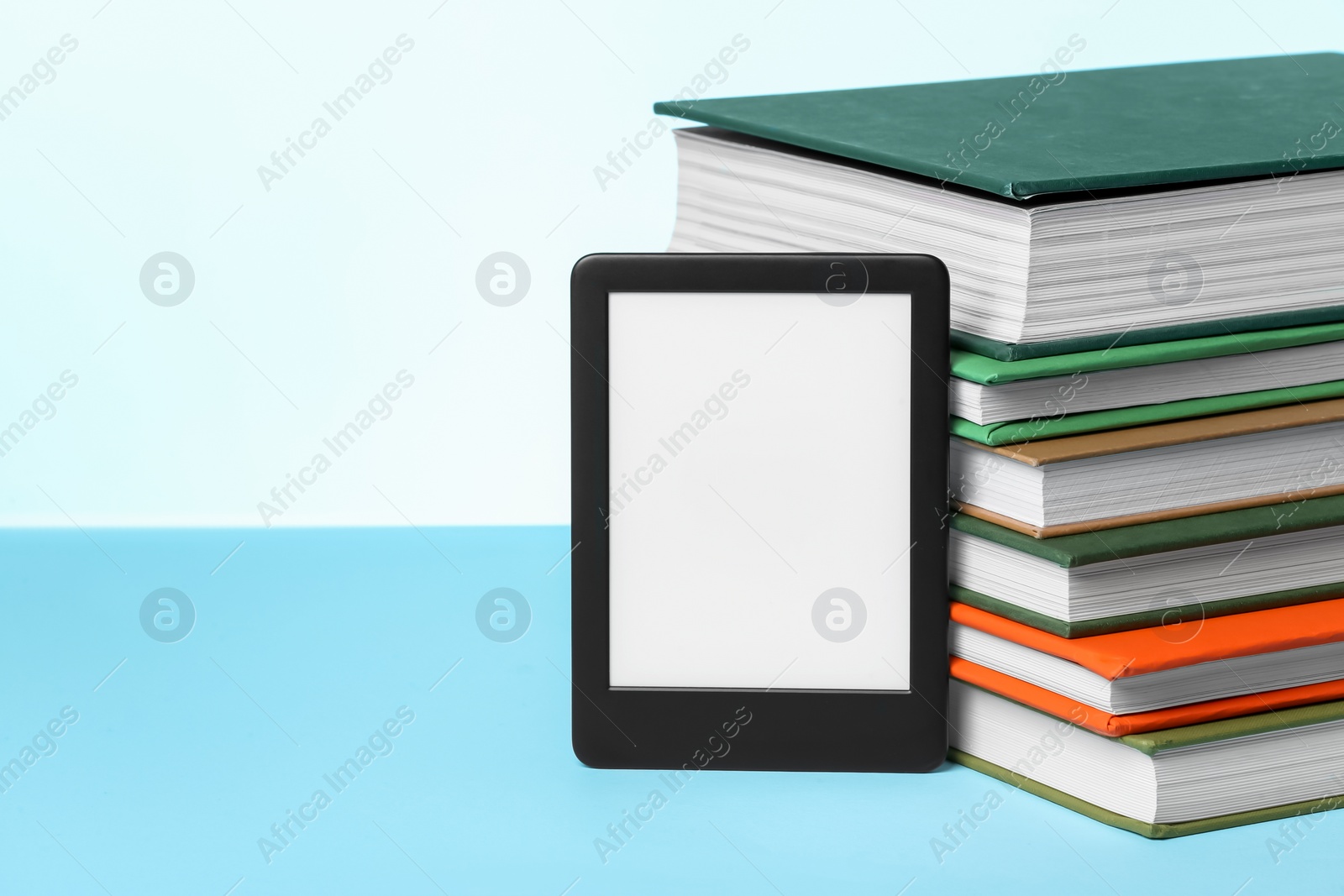 Photo of Modern e-book reader and stack of hard cover books on light blue background. Space for text