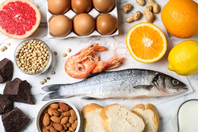 Flat lay composition of different products on white marble table. Food allergy concept