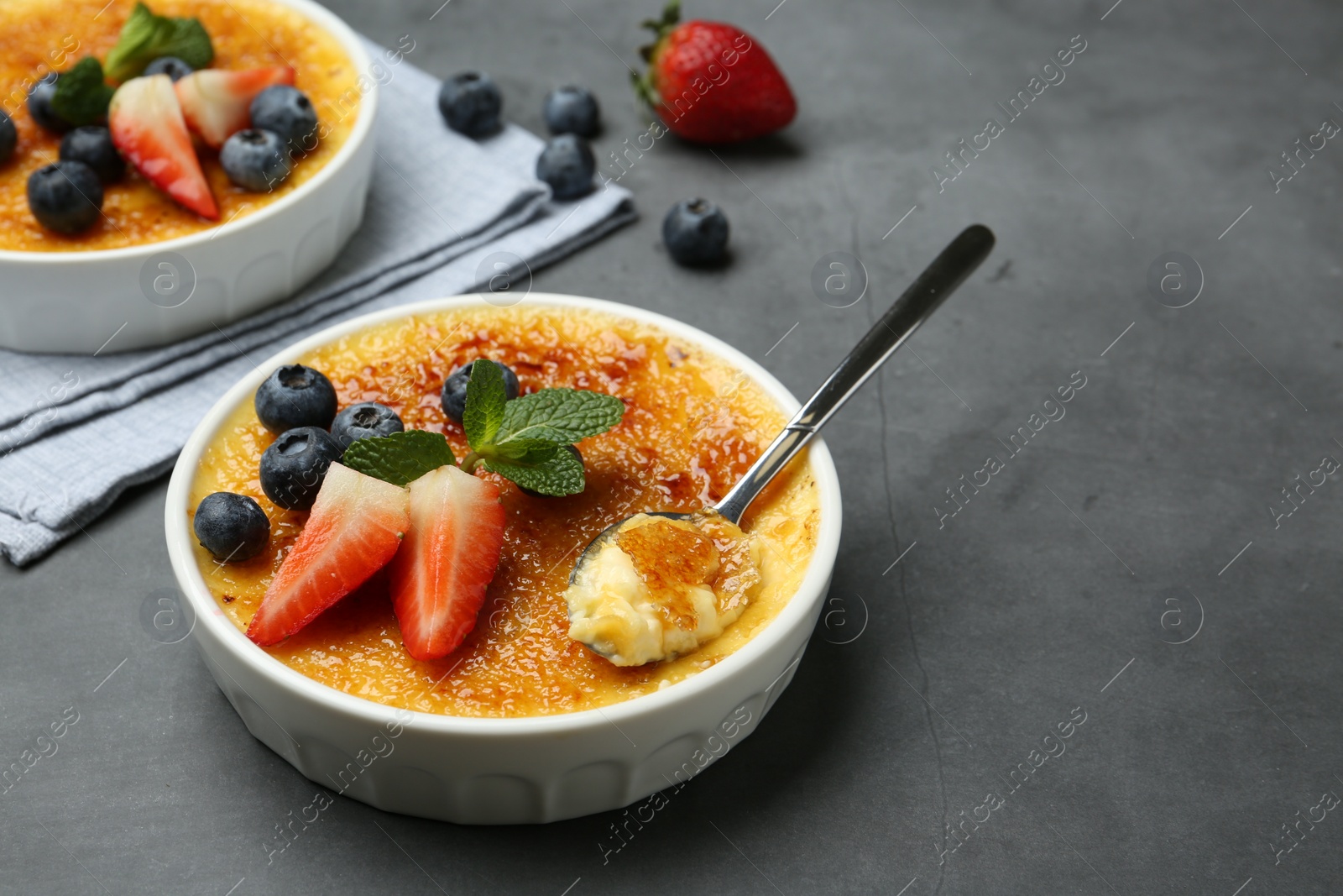 Photo of Delicious creme brulee with berries in bowl and spoon on grey table. Space for text