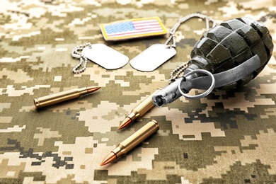 Photo of Military ID tags, grenade and rifle bullets on camouflage background