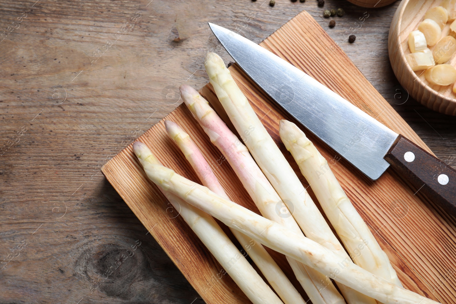 Photo of Fresh white asparagus, cutting board and knife on wooden table, flat lay