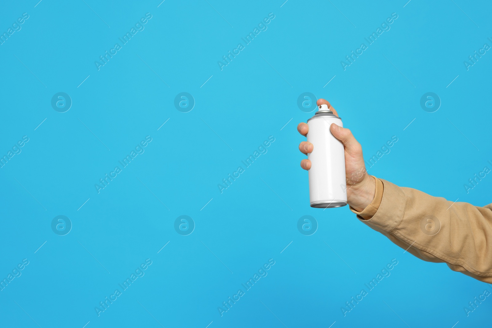 Photo of Man holding white can of spray paint on light blue background, closeup. Space for text