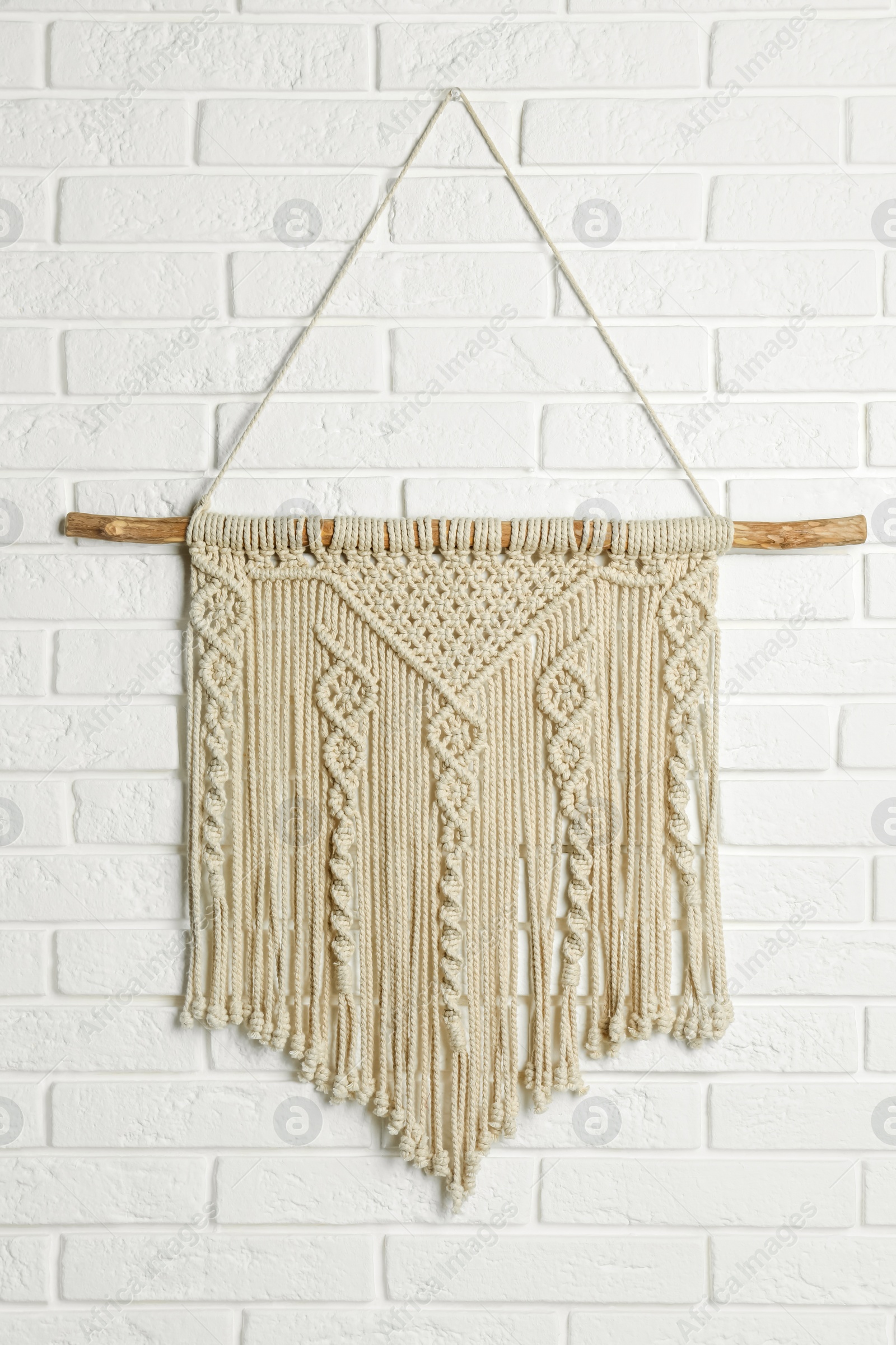 Photo of Beautiful macrame hanging on white brick wall. Decorative element