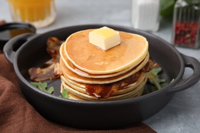 Tasty pancakes with butter, fried bacon and fresh arugula on grey table