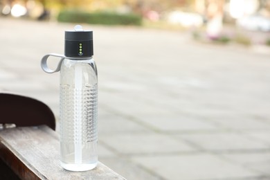Photo of Sport bottle of water on wooden bench outdoors, space for text