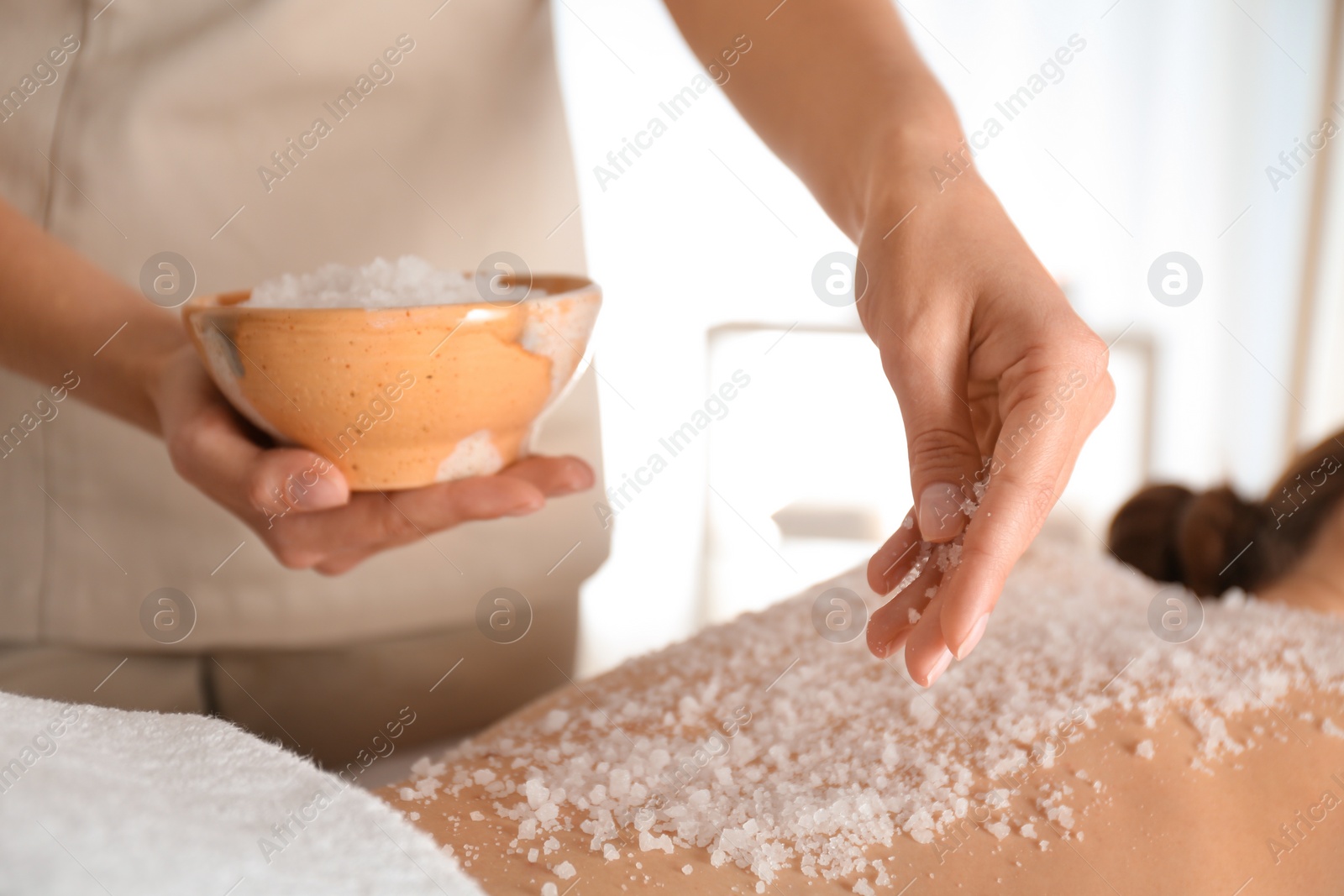 Photo of Young woman having body scrubbing procedure with sea salt in spa salon, closeup