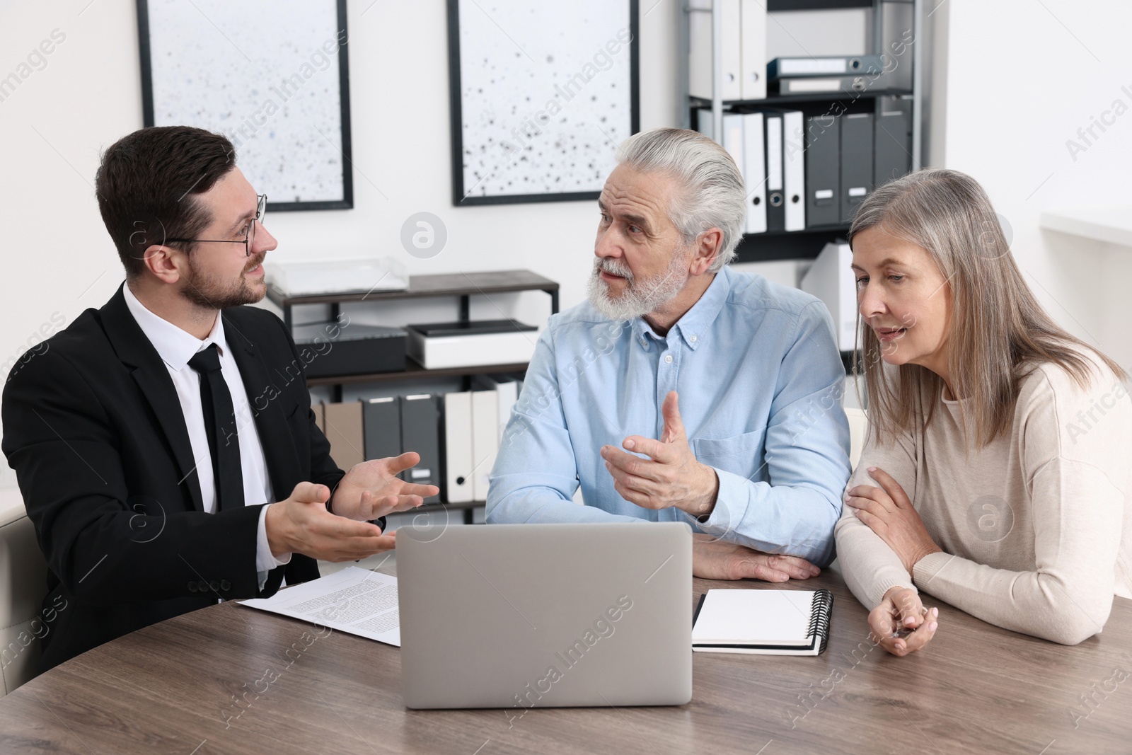 Photo of Insurance agent consulting elderly couple about pension plan at wooden table in office