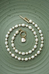 Photo of Elegant pearl necklace on olive textured background, top view