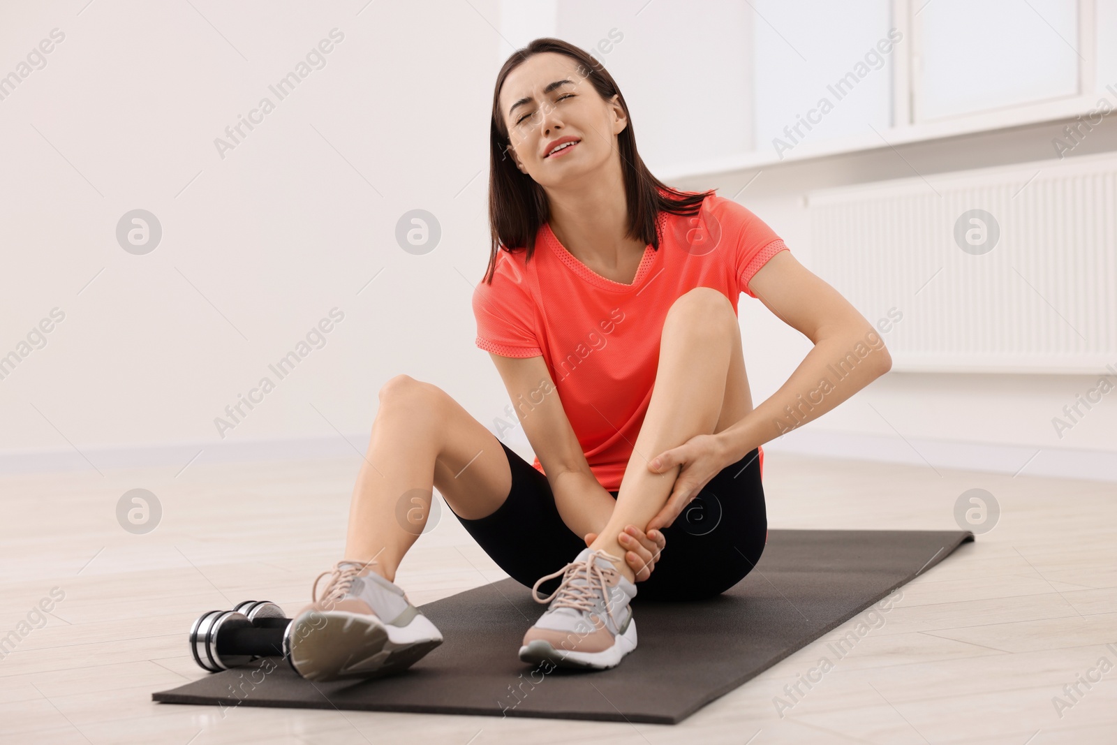 Photo of Young woman suffering from leg pain on exercise mat indoors