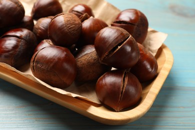 Photo of Fresh edible sweet chestnuts in serving plate on light blue wooden table, closeup