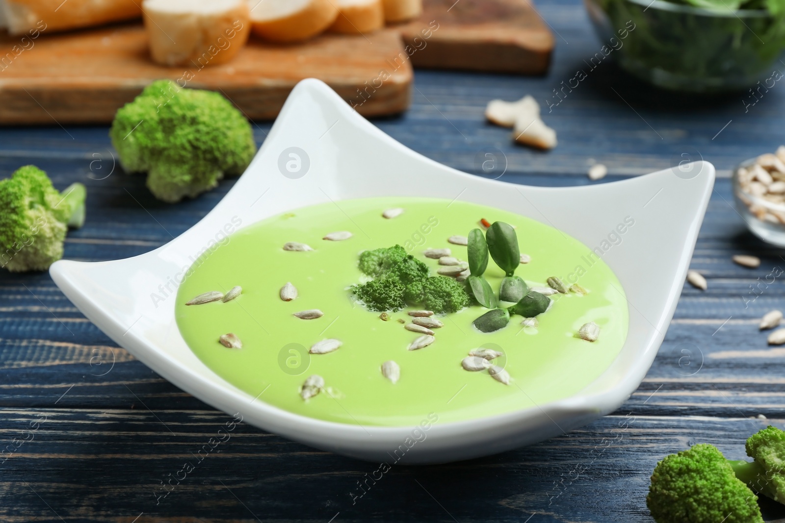 Photo of Bowl of cheese cream soup with broccoli and sunflower seeds served on blue wooden table