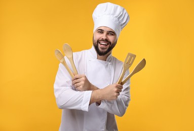 Photo of Happy young chef in uniform holding wooden utensils on orange background