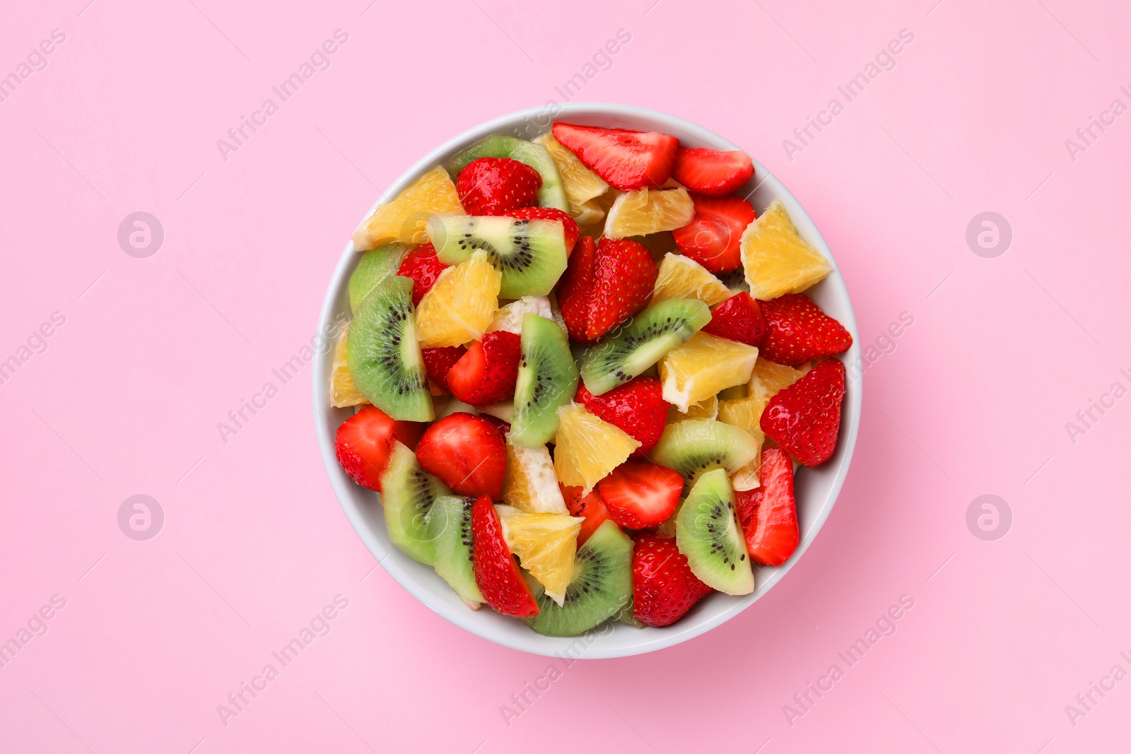 Photo of Yummy fruit salad in bowl on pink background, top view