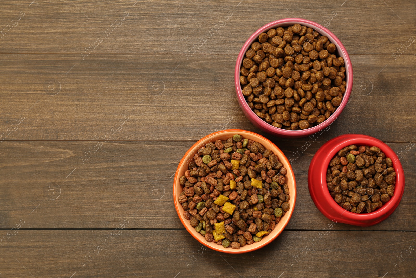 Photo of Dry food in pet bowls on wooden background, flat lay. Space for text