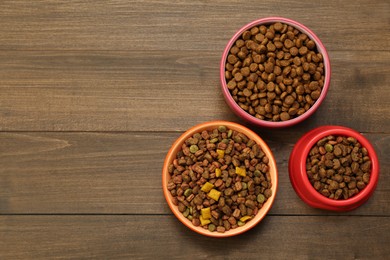 Photo of Dry food in pet bowls on wooden background, flat lay. Space for text