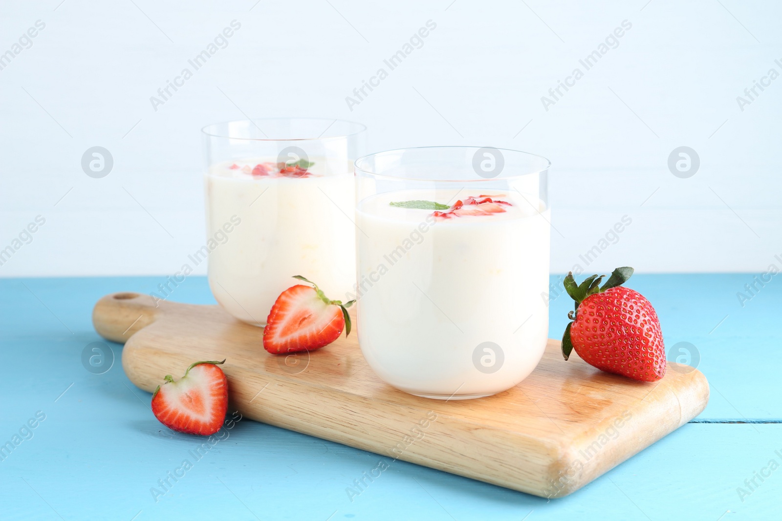 Photo of Tasty yogurt in glasses and strawberries on light blue wooden table