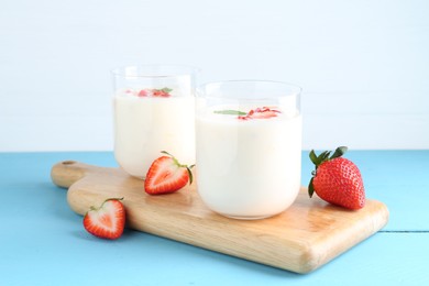 Tasty yogurt in glasses and strawberries on light blue wooden table