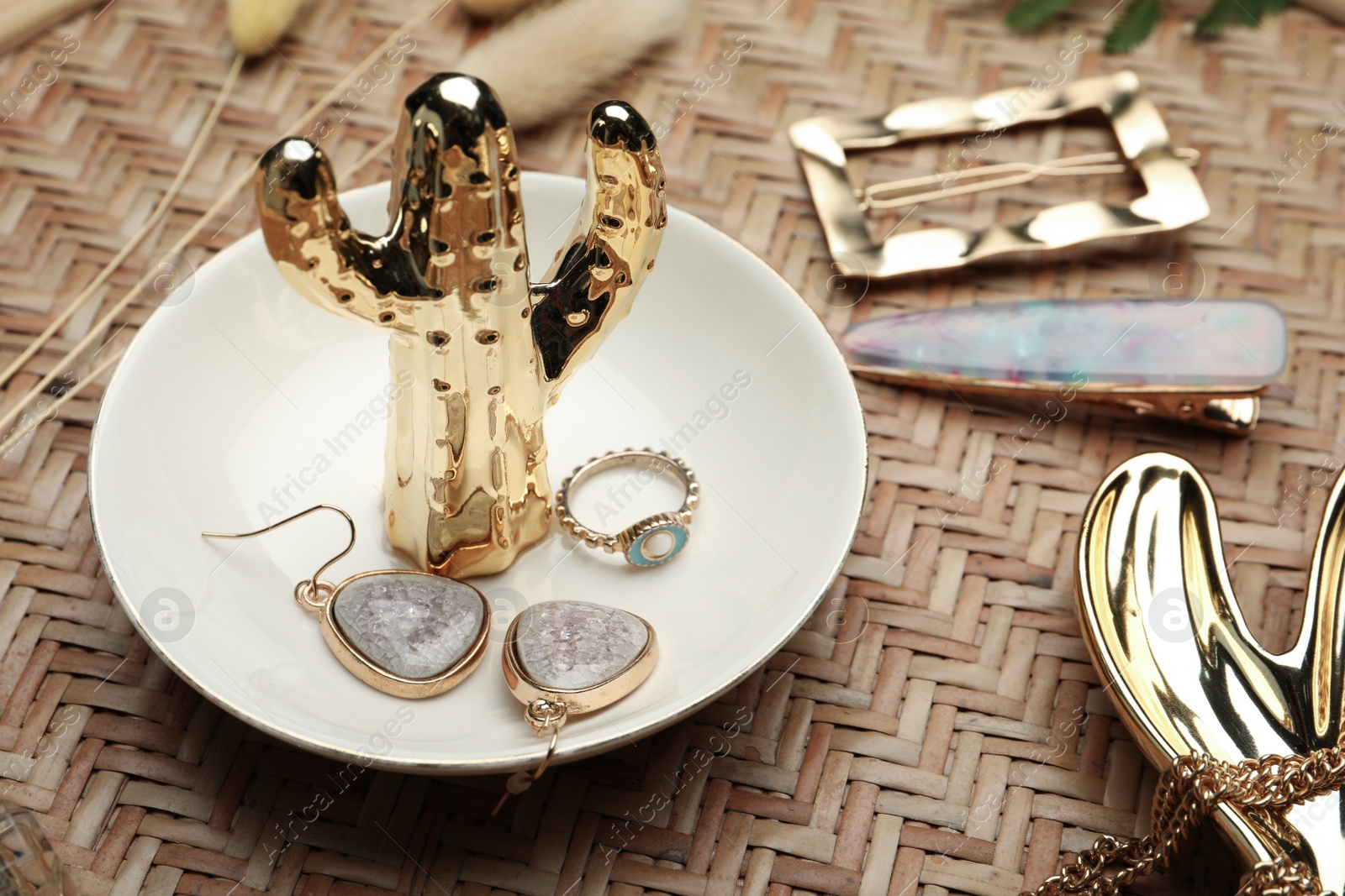 Photo of Stylish golden bijouterie and decorative cactus on wicker table, closeup