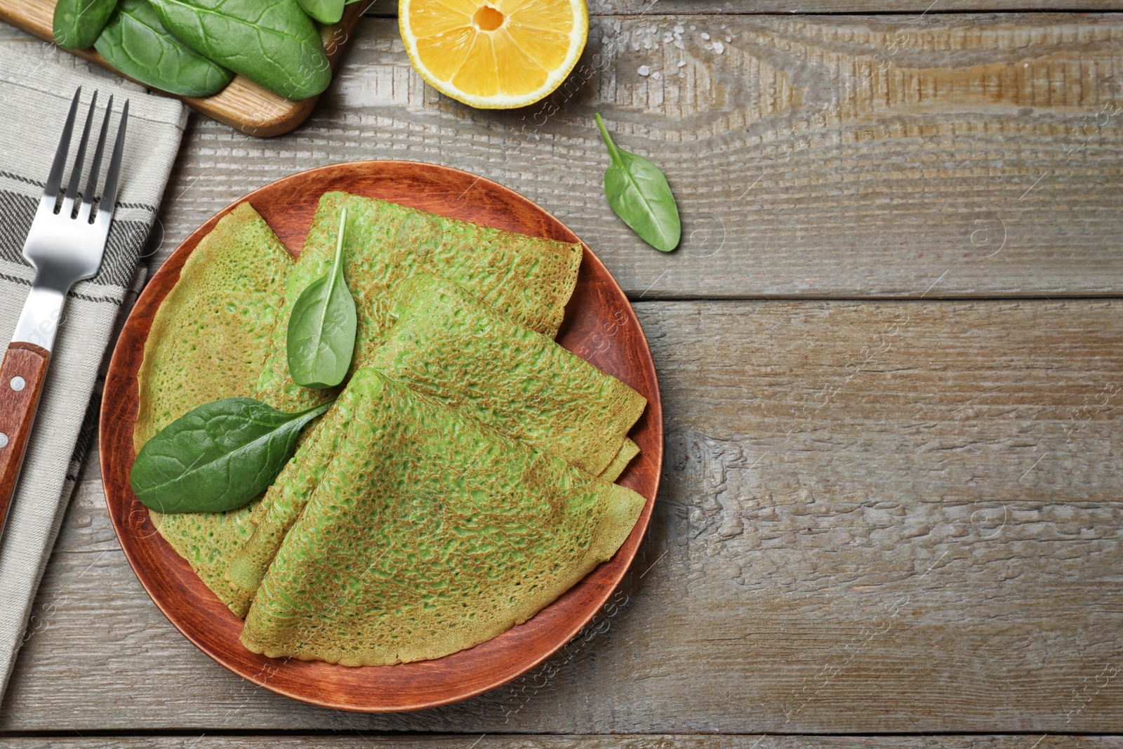 Photo of Delicious spinach crepes served on wooden table, flat lay. Space for text