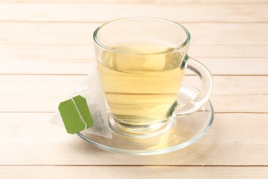 Photo of Tea bag and glass cup on light wooden table, closeup