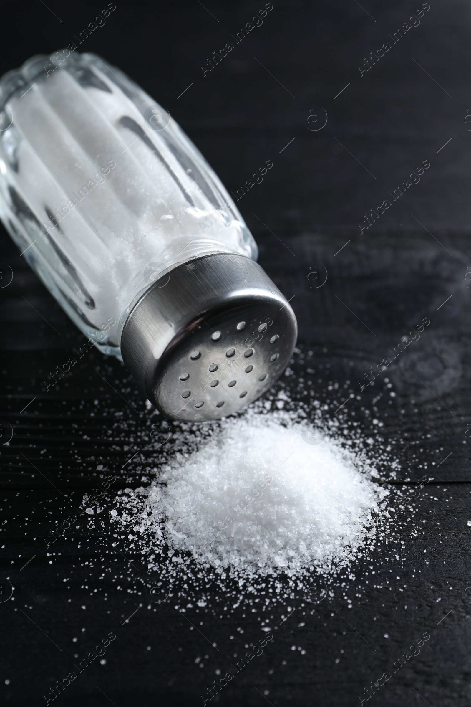 Photo of Organic salt in glass shaker on black wooden table, closeup