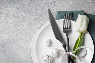 Festive table setting with painted eggs and white tulip on light grey background, top view with space for text. Easter celebration