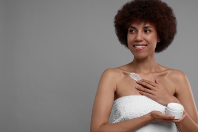 Beautiful young woman applying cream onto body on grey background, space for text