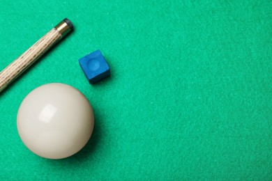Photo of White billiard ball, chalk and cue on green table, flat lay. Space for text