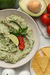 Delicious guacamole with nachos chips and ingredients on white table, flat lay