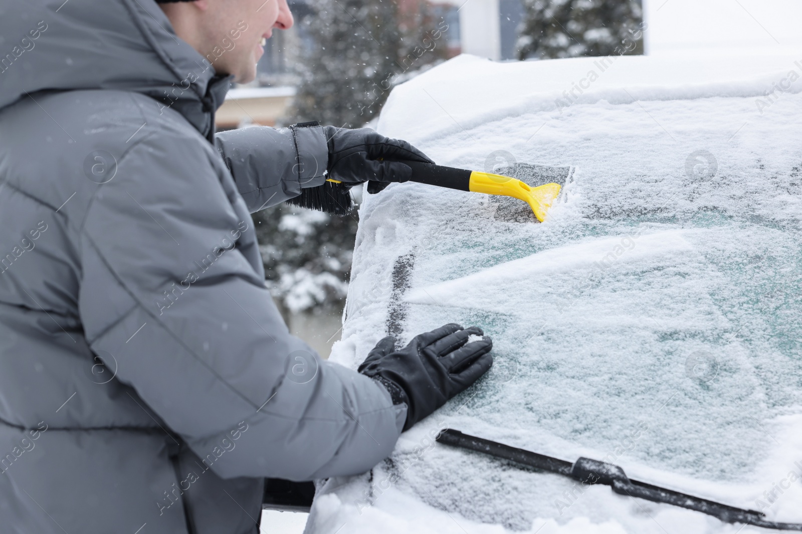 Photo of Man cleaning snow from car windshield outdoors, closeup