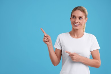 Photo of Special promotion. Smiling woman pointing at something on light blue background. Space for text