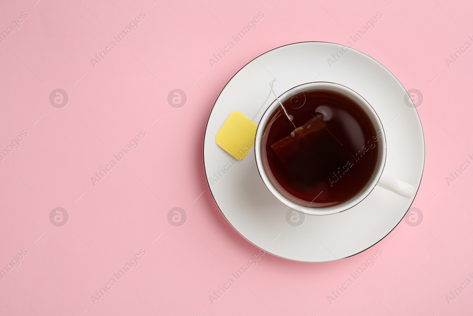 Photo of Tea bag in cup of hot water on pink background, top view. Space for text