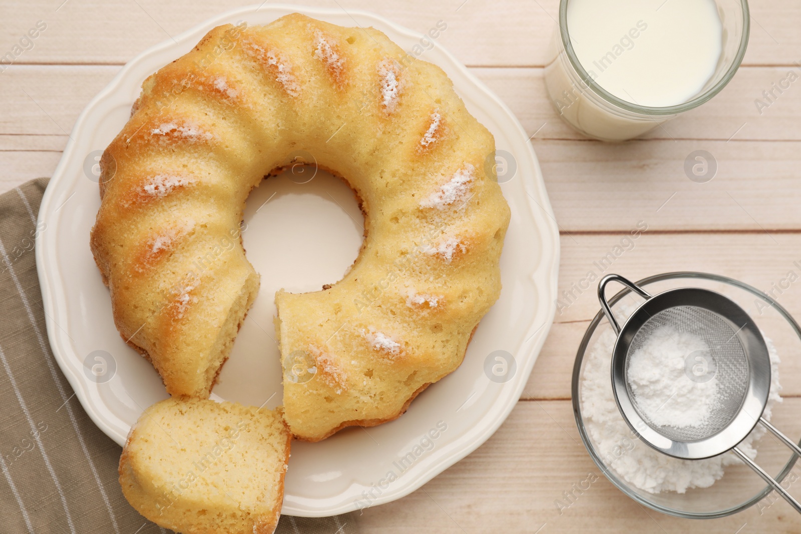 Photo of Delicious sponge cake with powdered sugar and glass of milk on wooden table, flat lay