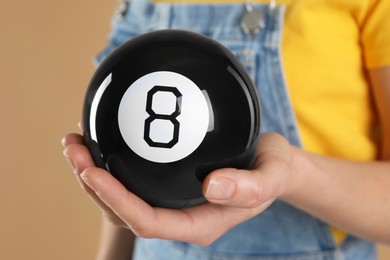 Woman holding magic eight ball on light brown background, closeup