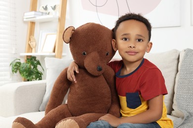 Cute African-American boy with big teddy bear at home