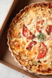 Photo of Tasty quiche with tomatoes and cheese in open box on light table, top view