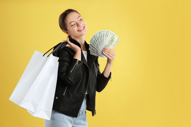 Photo of Young woman with money and shopping bags on yellow background. Space for text