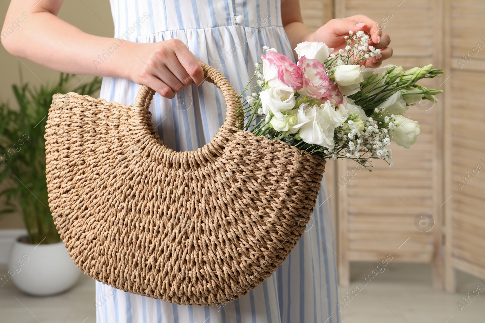 Photo of Woman holding beach bag with beautiful bouquet indoors, closeup