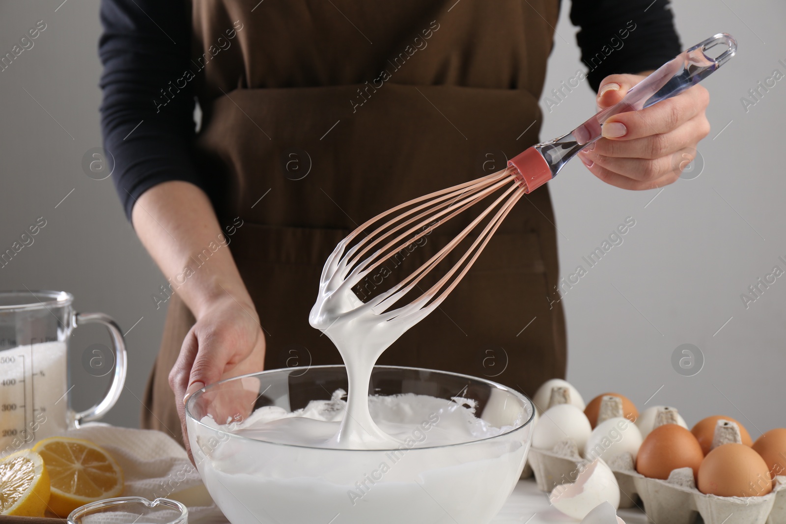 Photo of Woman making whipped cream with whisk at table, closeup