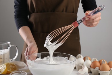 Woman making whipped cream with whisk at table, closeup